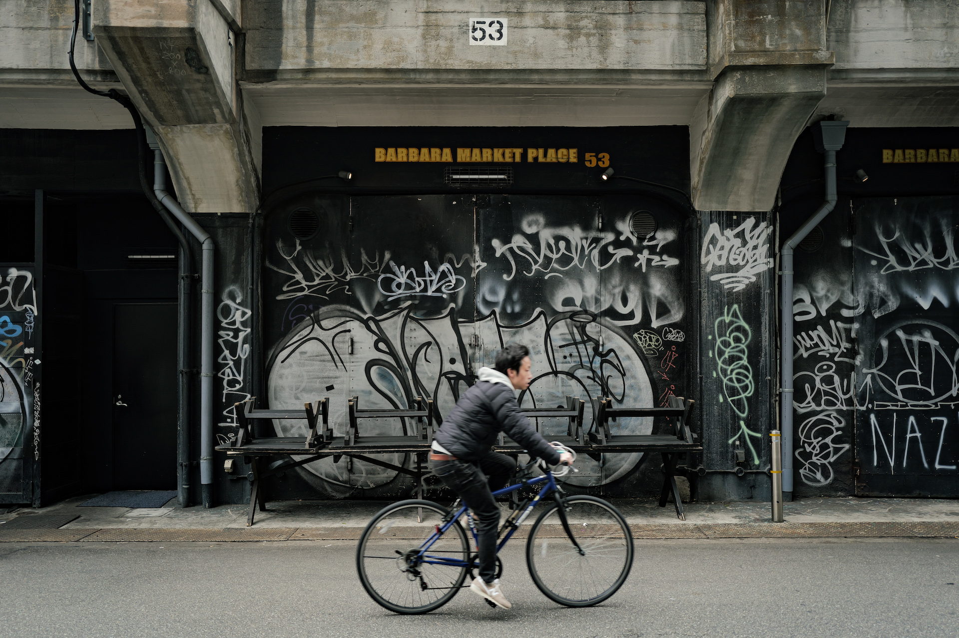 Leica Q3で撮影した作例　落書きされた高架下を横切る自転車に乗る男性